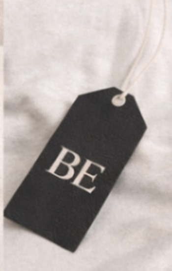 Black swing tag with a foil BE mark on a corded loop